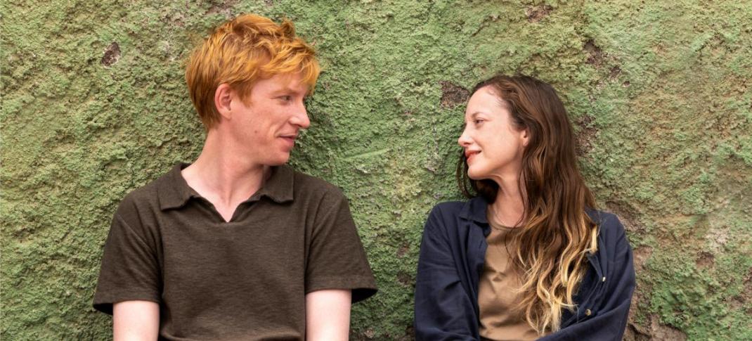Domhnall Gleeson as Jack and Andrea Riseborough as Alice sit against a wall gazing at each other in 'Alice & Jack'